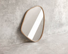 ELE125 Mirror with organic shape and gold frame against concrete wall.