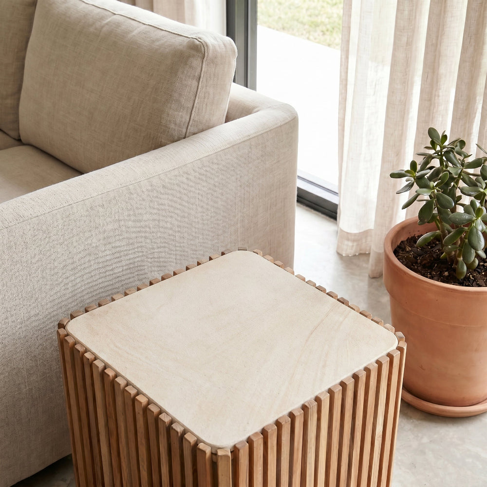 Wooden side table with beige cushion next to a beige sofa and potted plant.