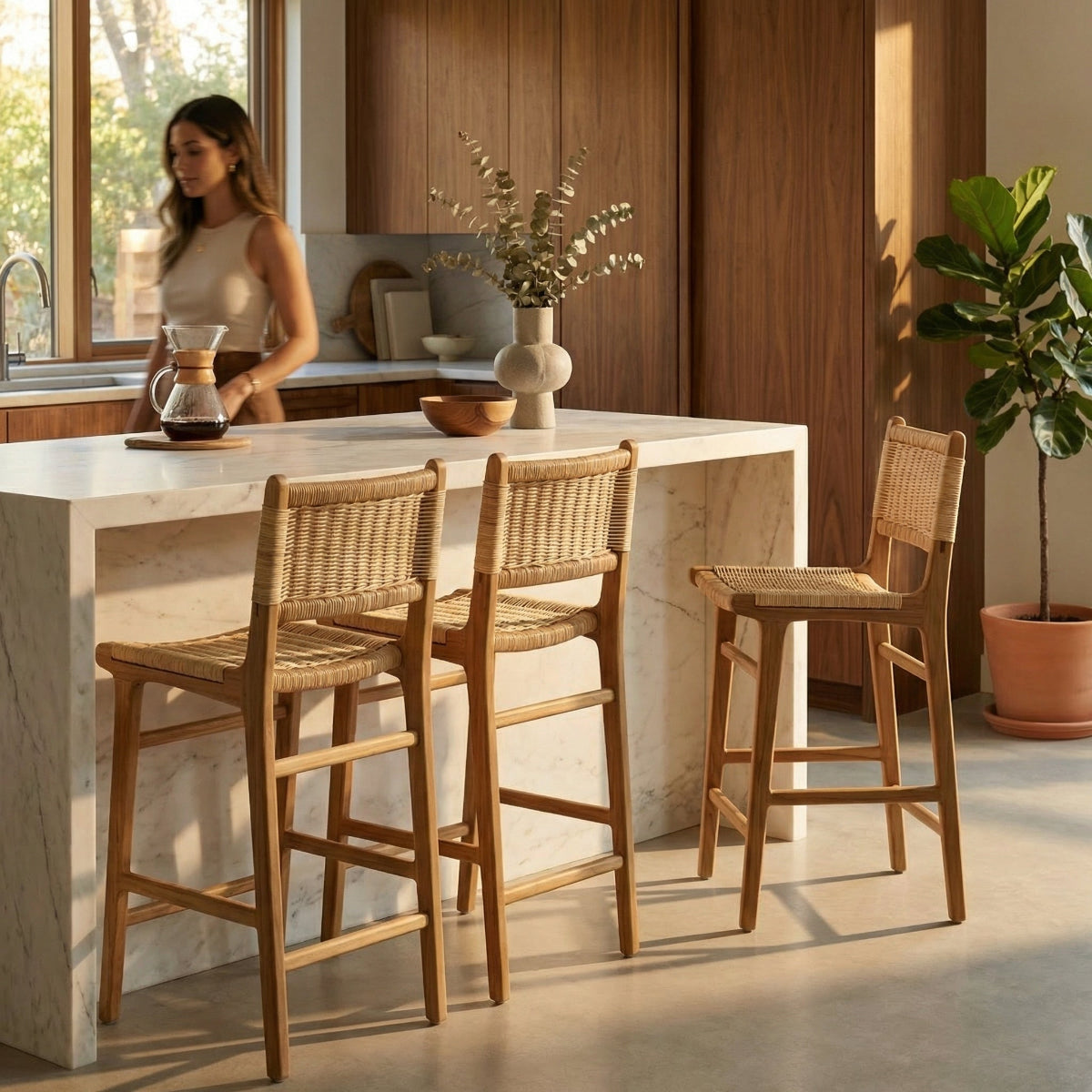 Kitchen with marble island and wooden bar stools, woman standing by window