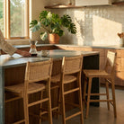Person using a coffee maker at a kitchen island with wicker chairs.