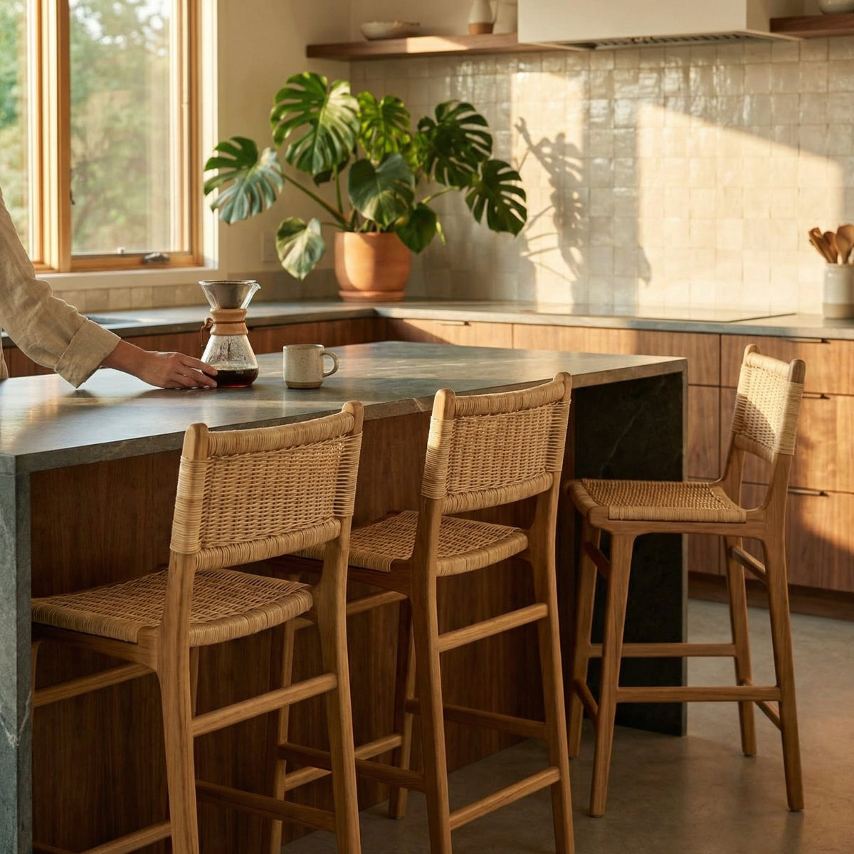 Person using a coffee maker at a kitchen island with wicker chairs.