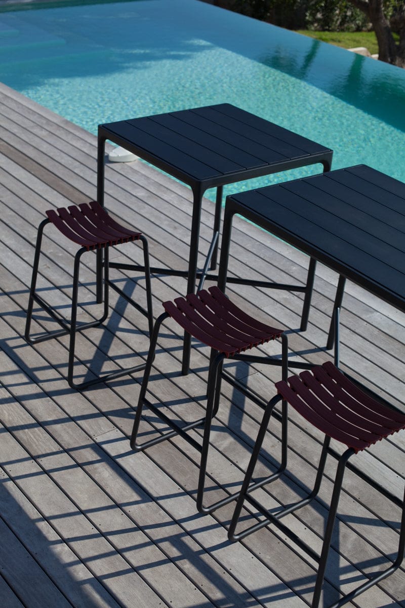 Outdoor bar set with black tables and burgundy stools.