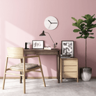 Pink office desk with chair, clock, and plant.