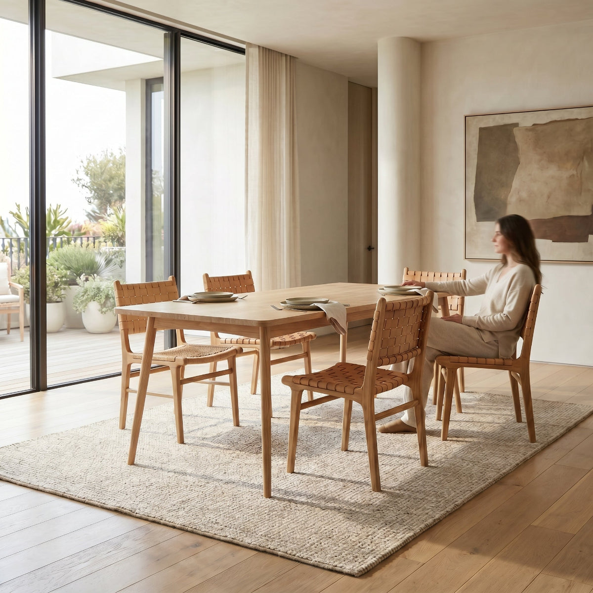 Woman sitting at a wooden dining table in a modern living room with large windows.