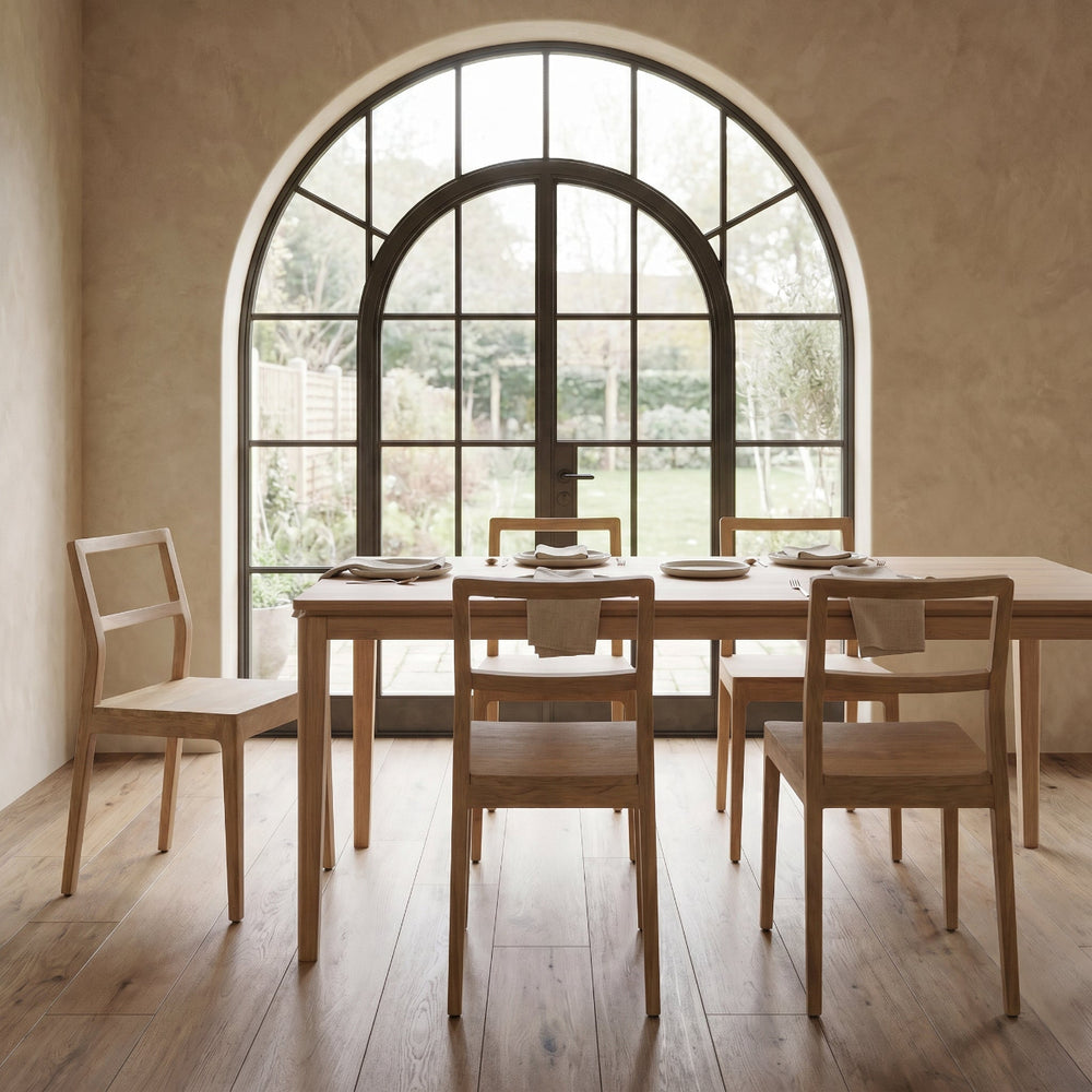 Dining area with wooden table and chairs in front of a large arched window.