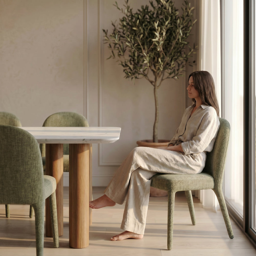 Woman sitting in a modern dining room with a tree and large window.