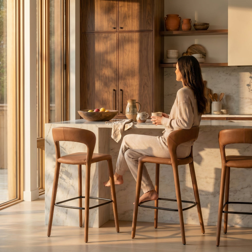 Woman sitting at a kitchen counter with wooden stools in a bright, modern kitchen.