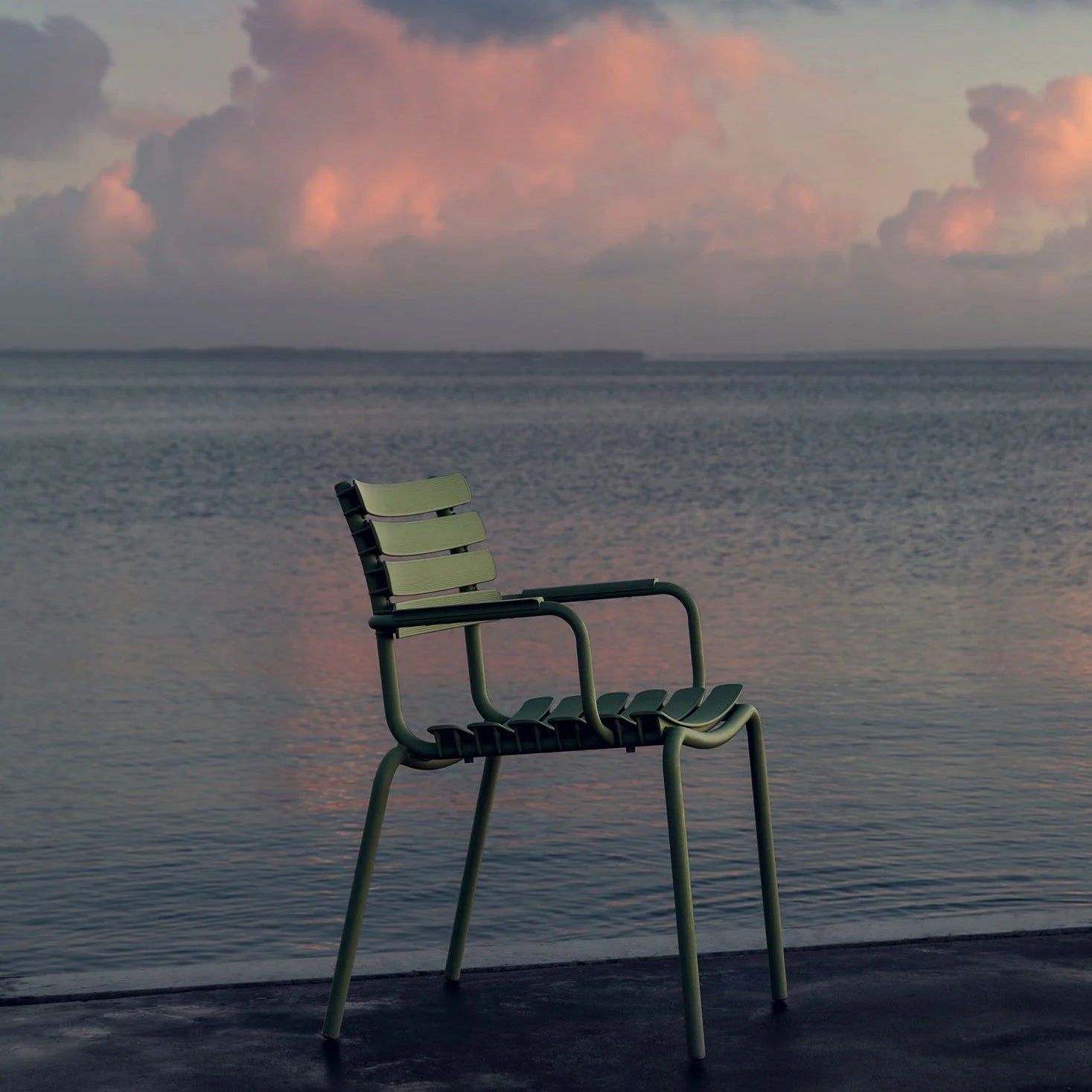 Chair on a deck overlooking a calm sea with a sunset sky.