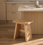Wooden stool in a kitchen setting with light wood cabinets and a countertop.