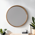 Round wooden-framed mirror on a white wall with decorative items below.