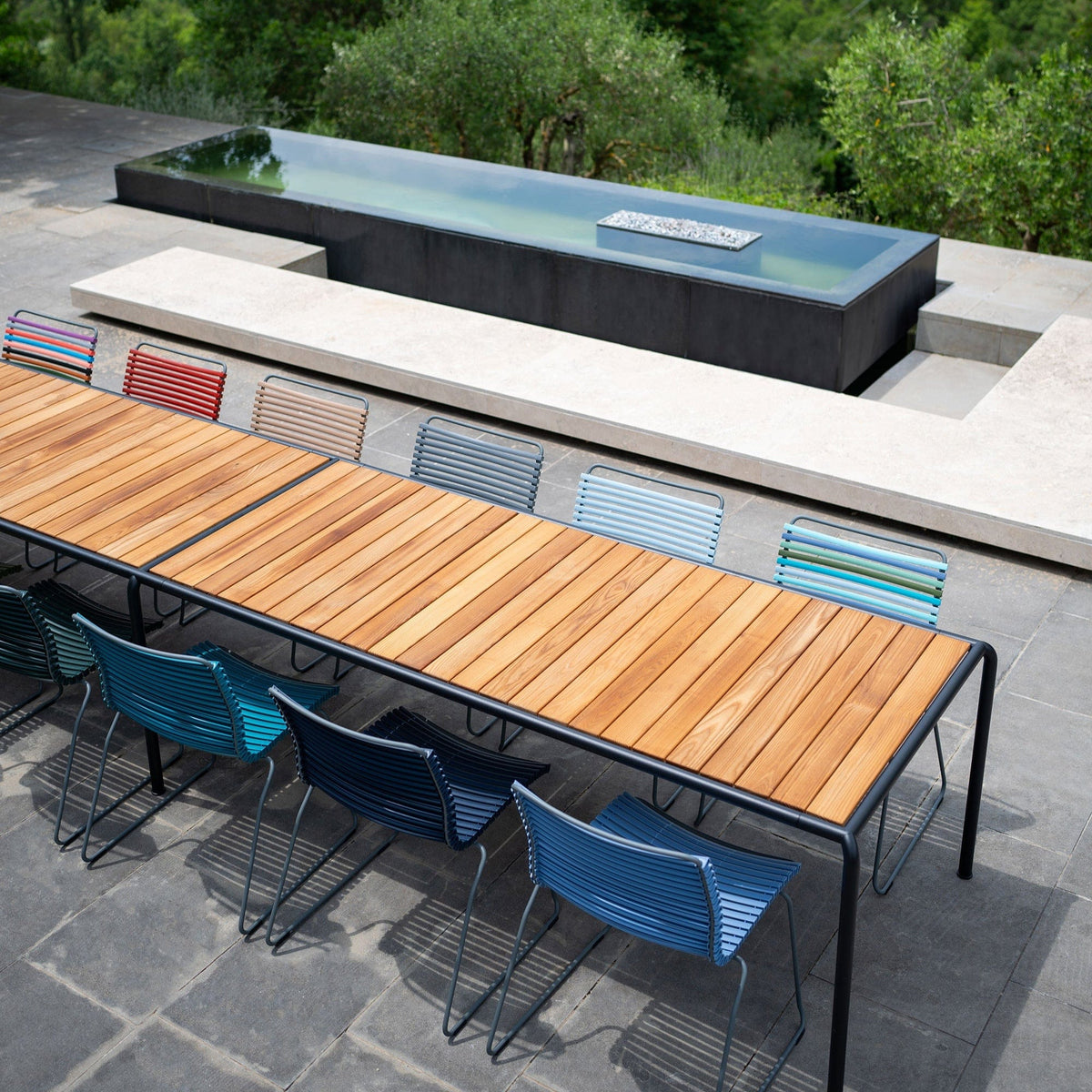 Outdoor dining table with no-arm chairs near pool.