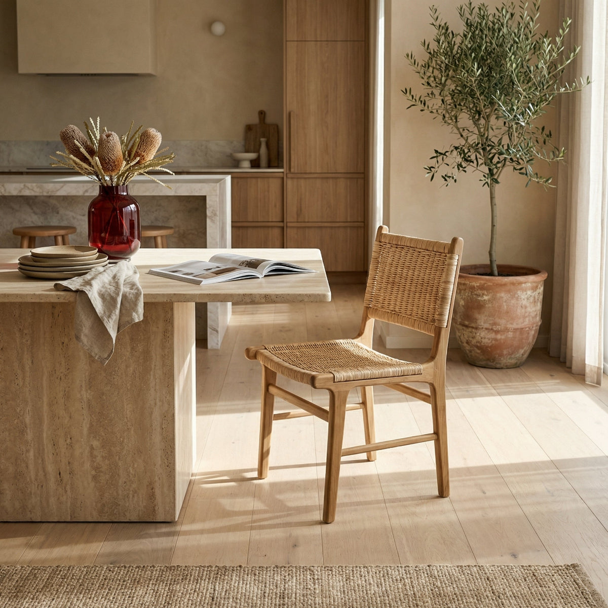 Dining area with a wooden table and chair, vase with dried plants, and potted plant in a neutral-toned room.