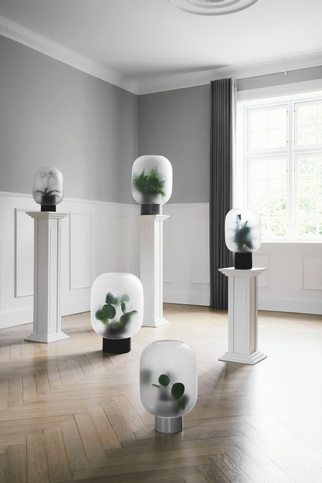 Glass lanterns with plants on white pedestals.