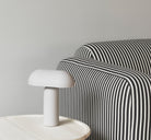 Gray table lamp on side table next to striped armchair.
